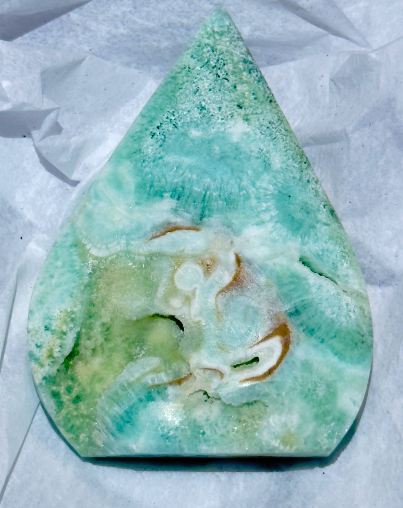 A teardrop-shaped Caribbean calcite freeform  polished stone cabochon with marbled green, aqua, cream, and brown veining
