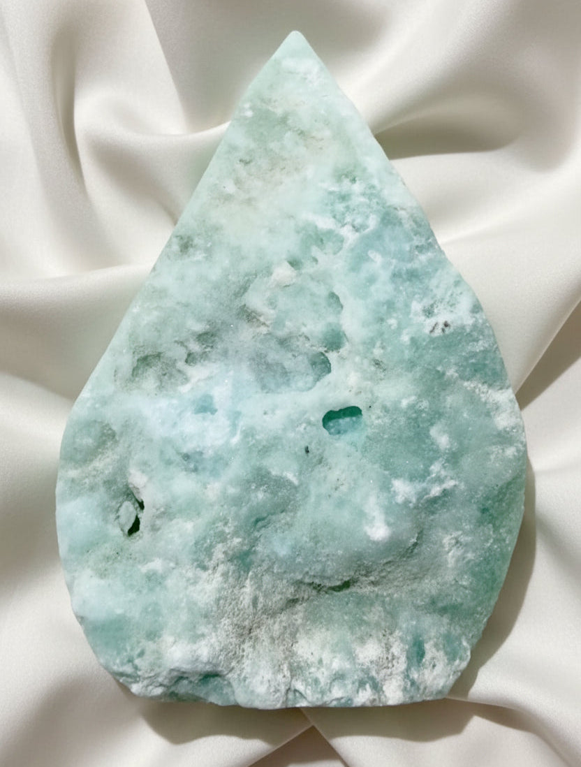 A raw, teardrop-shaped Caribbean calcite mineral specimen with natural mottled patterns of light green, white, and teal