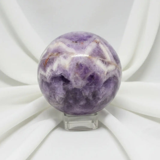 close up of a carved sphere chevron amethyst with iron inclusions soft white fabric backdrop 