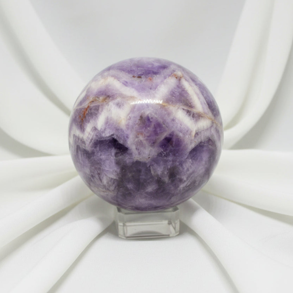 close up of a carved sphere chevron amethyst with iron inclusions soft white fabric backdrop 