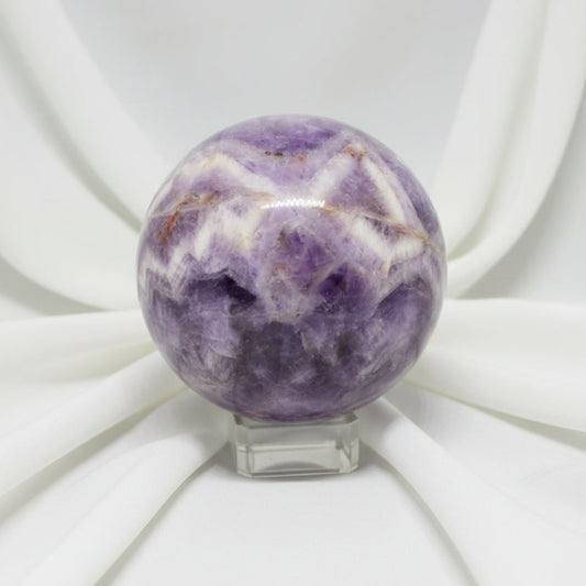 close up of a carved sphere chevron amethyst with iron inclusions soft white fabric backdrop 