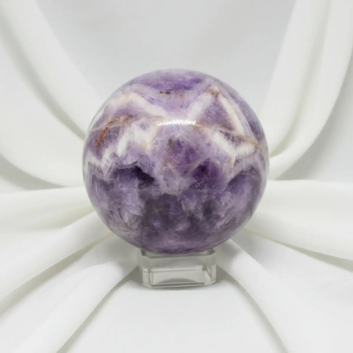 close up of a carved sphere chevron amethyst with iron inclusions soft white fabric backdrop 