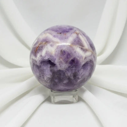 close up of a carved sphere chevron amethyst with iron inclusions soft white fabric backdrop 
