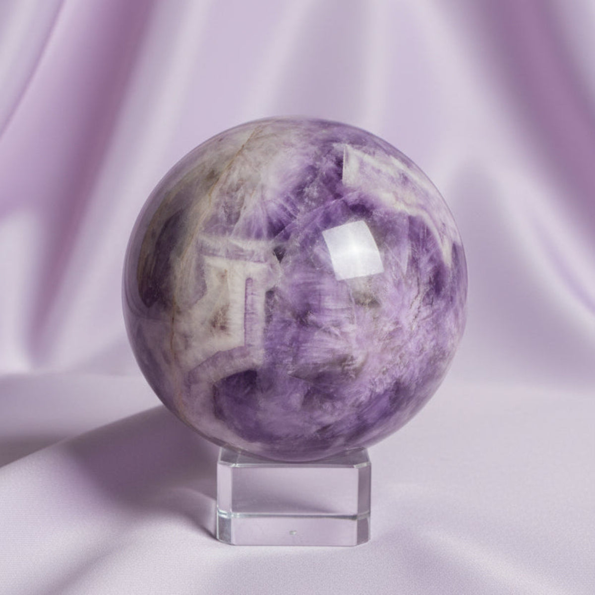 close up amethyst carved sphere light and dark purples, white and clear light lavender color fabric backdrop