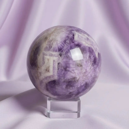 close up amethyst carved sphere light and dark purples, white and clear light lavender color fabric backdrop