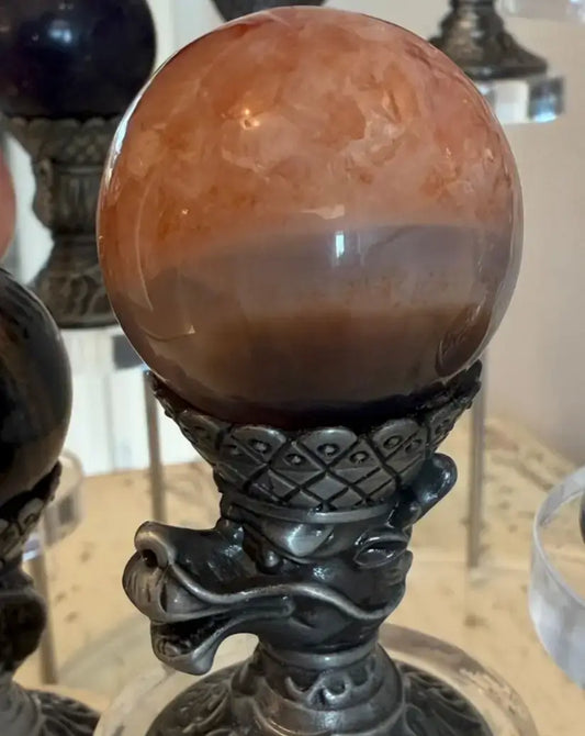 A polished carnelian sphere in a chinese zodiac dragon sphere display made from brass