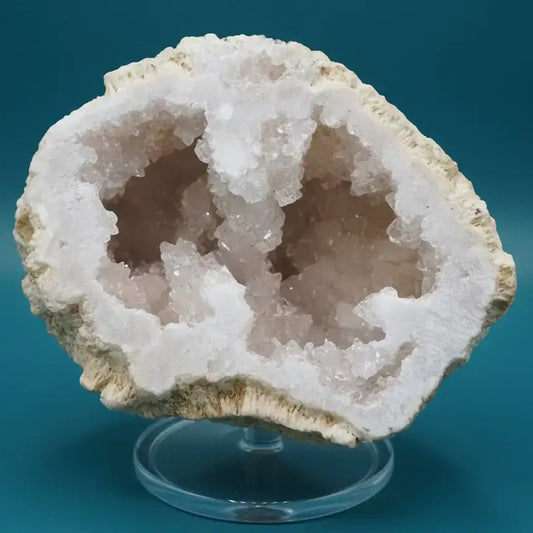 Clear Quartz Geode showing white shimmer Specimen on a stand with a blue background