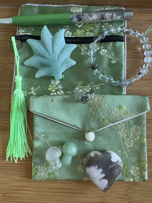 Overhead shot of green pouches with gemstone jewelry, a green pen, a tassel, and carved stones.
