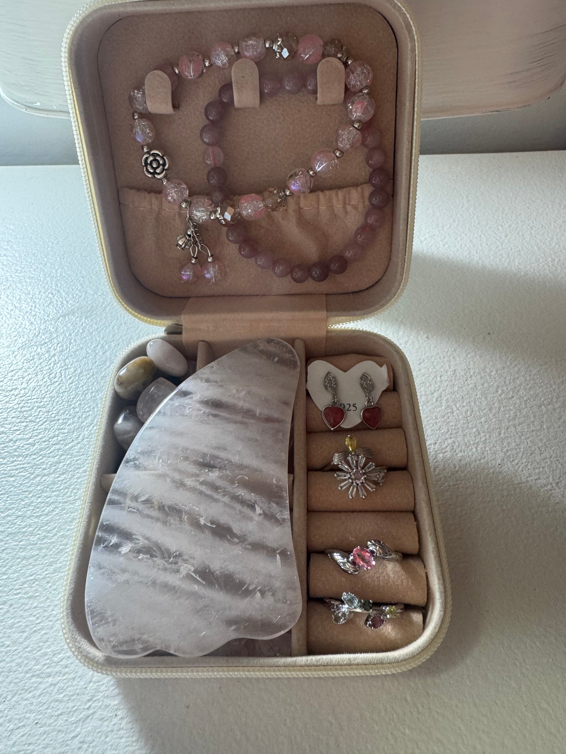 An open jewelry box displaying rings, earrings, bracelets, tumbled stones, and a gua sha.