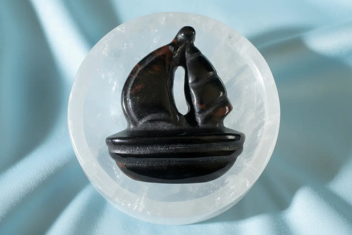 Carved obsidian sailboat on a selenite bowl.