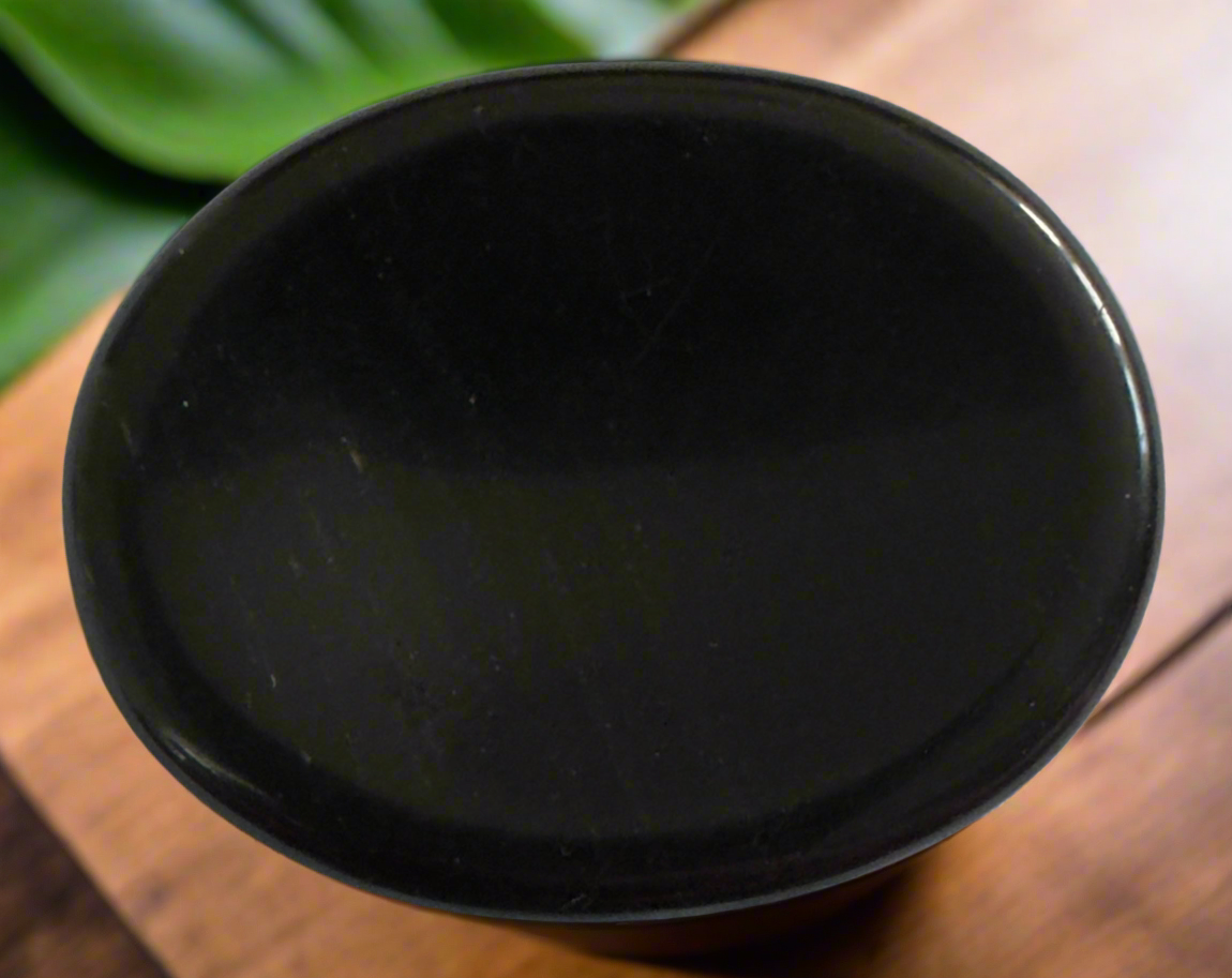 Close-up of a shiny, black container on a wooden surface, with green leaves visible in the background.
