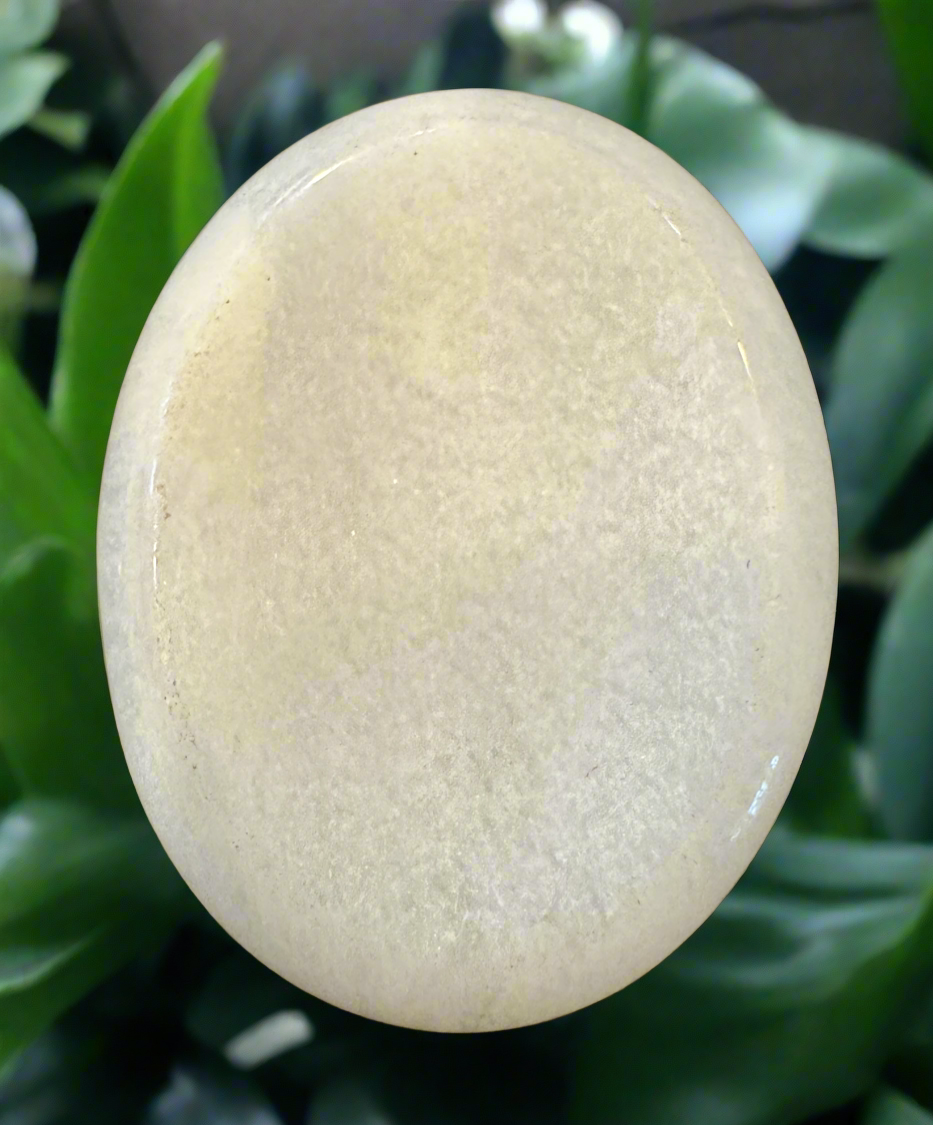 An opaque, yellowish-white stone sphere is set against a backdrop of green foliage.