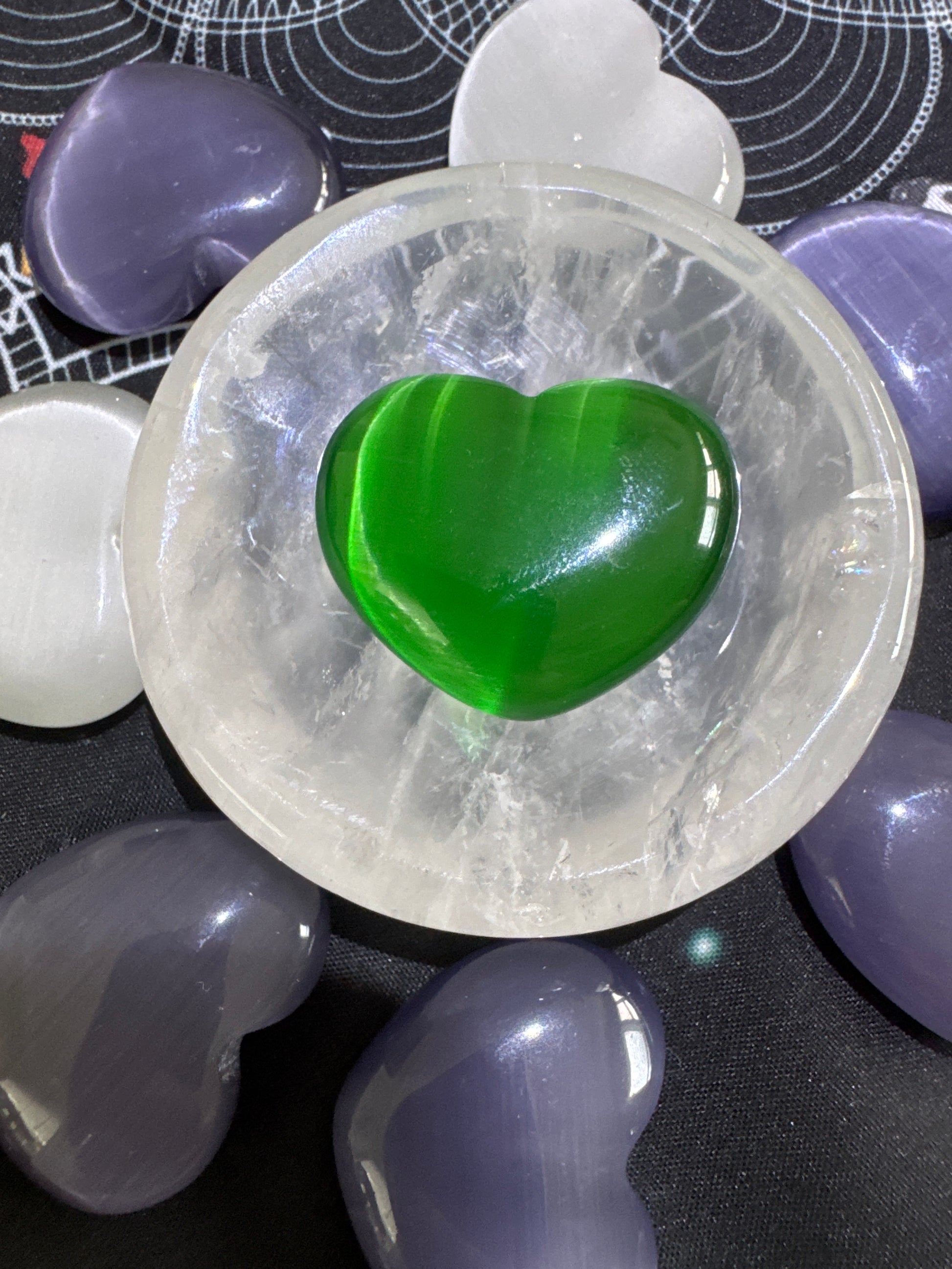 Overhead shot of green and purple heart-shaped crystals arranged around a clear quartz bowl containing a green heart-shaped crystal.