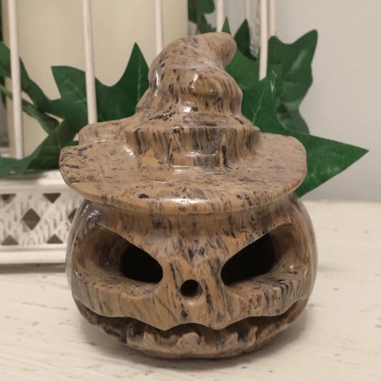 Dendritic Jasper Carved Jack O’Lantern sitting on a white table with greenery behind it