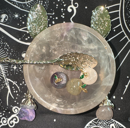 Overhead shot of a crystal bowl containing apple-shaped stones, silver spoons with floral designs on a black and white patterned cloth.

