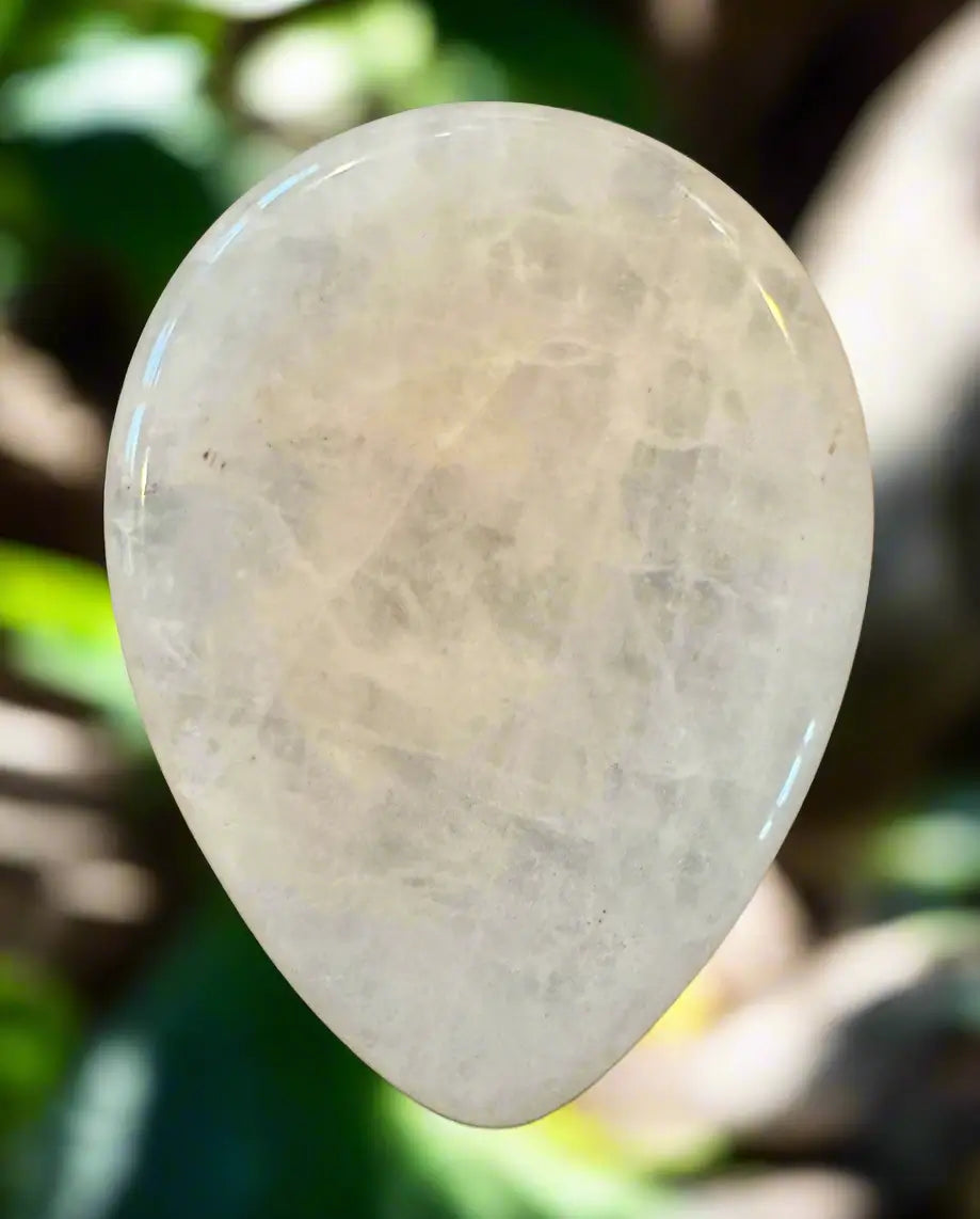 Translucent pearlescent teardrop-shaped gemstone, blurred green background.