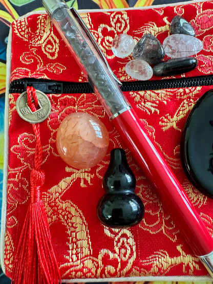 Red fabric pouch with gold pattern, red tassel, pen, crystals, and black gourd.