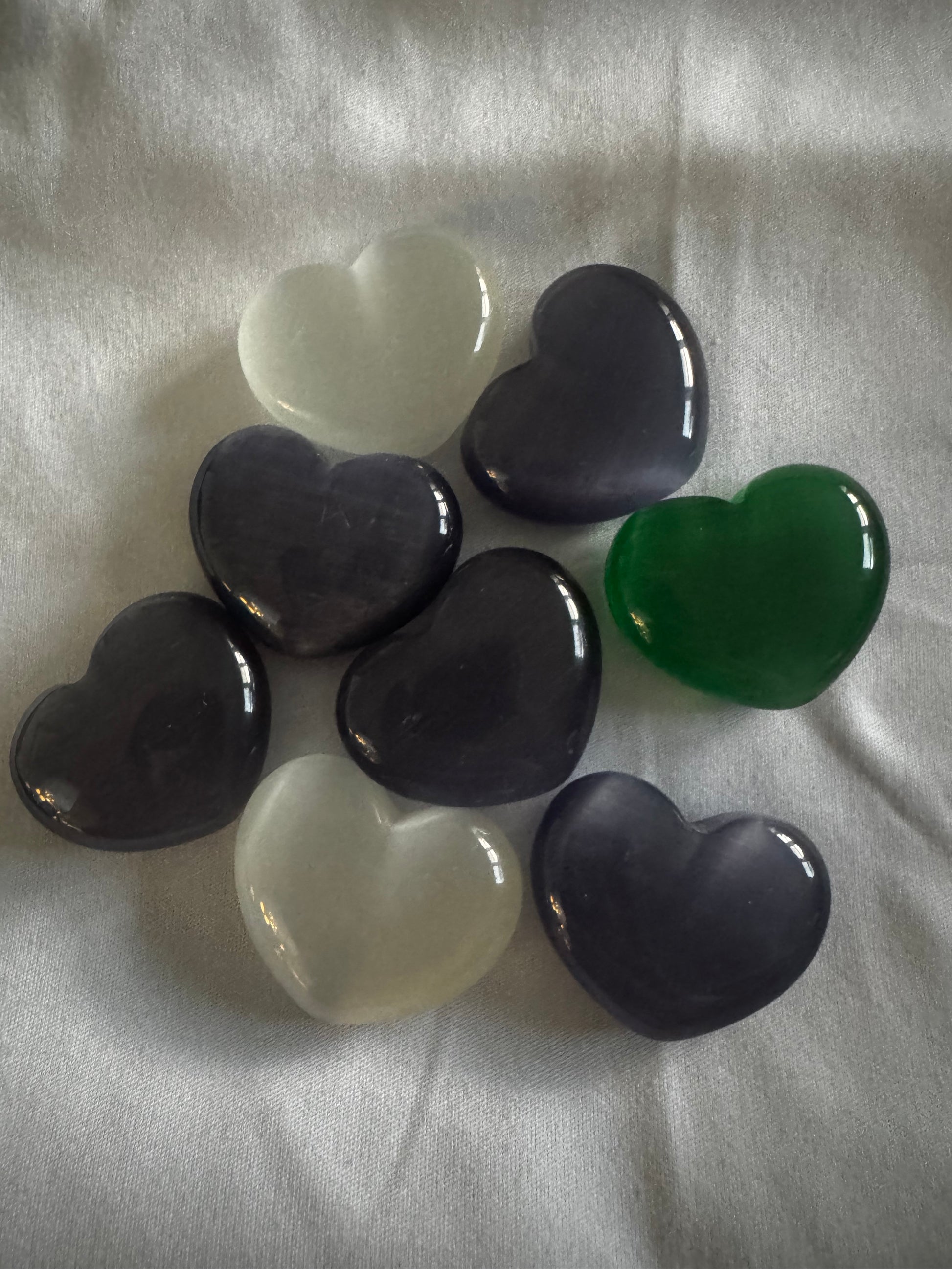 Eight heart-shaped gemstones in white, purple, dark purple, and green on a white fabric. 
