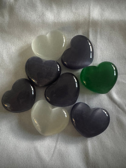 Eight heart-shaped gemstones in white, purple, dark purple, and green on a white fabric. 
