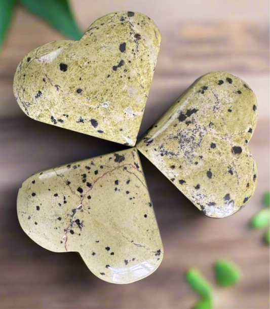Three heart-shaped stones in a clover arrangement. They are light green with black speckles. Wood background, blurry green foliage in the background.