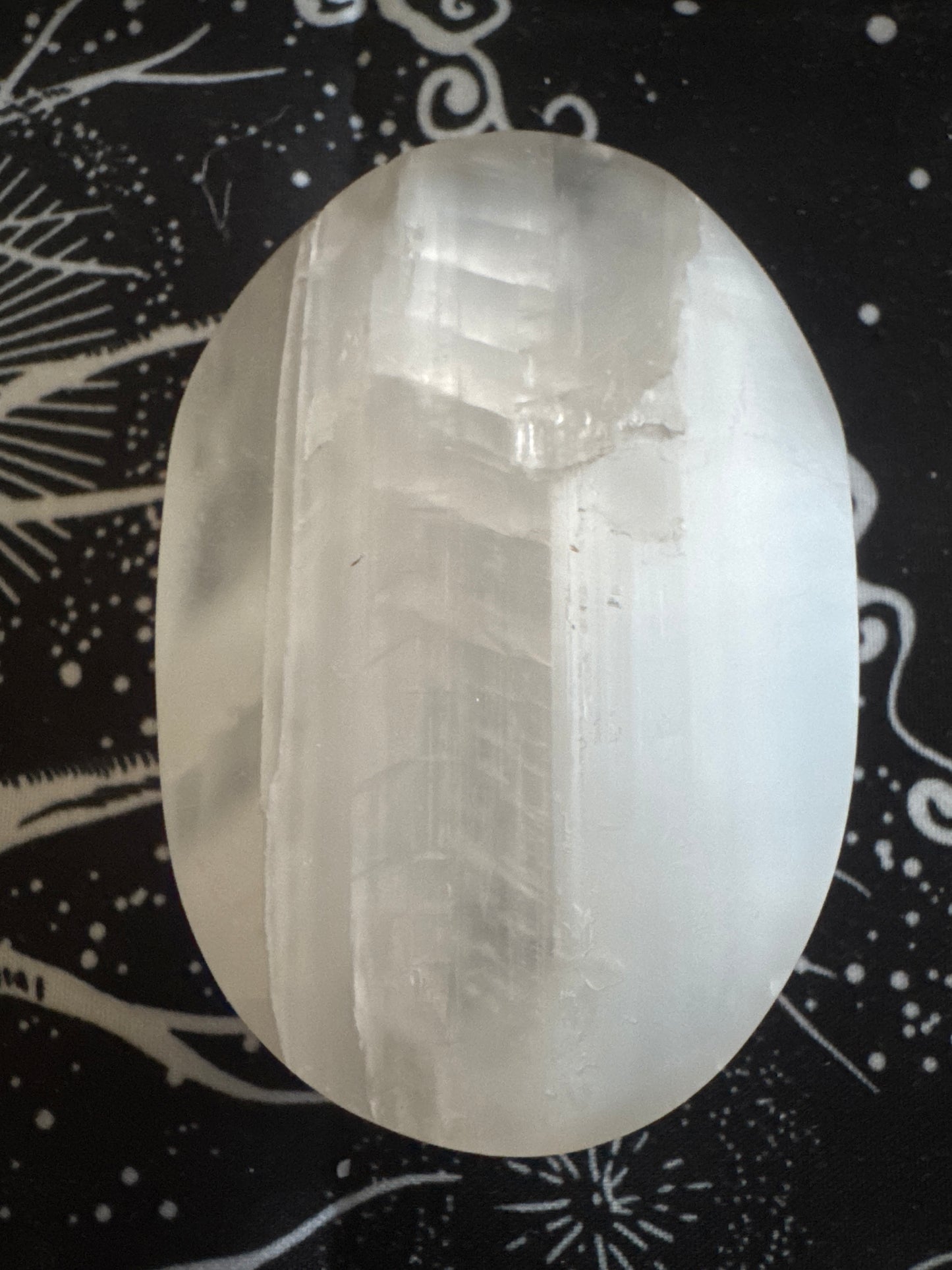 Selenite palm stone on a black and white tapestry.
