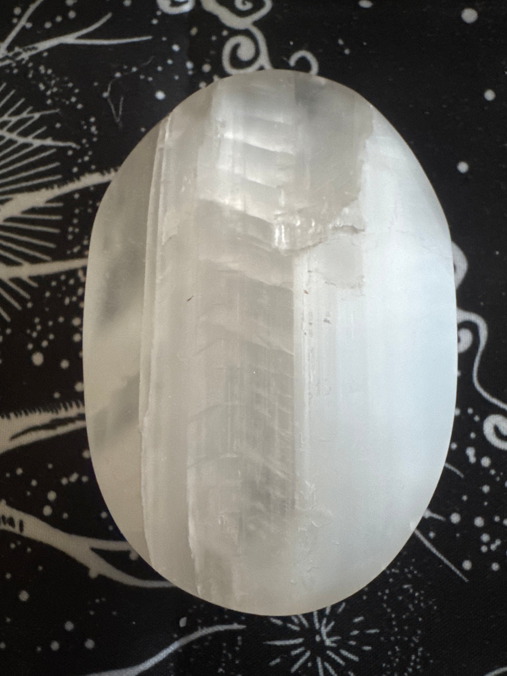 Selenite palm stone on a black and white tapestry.