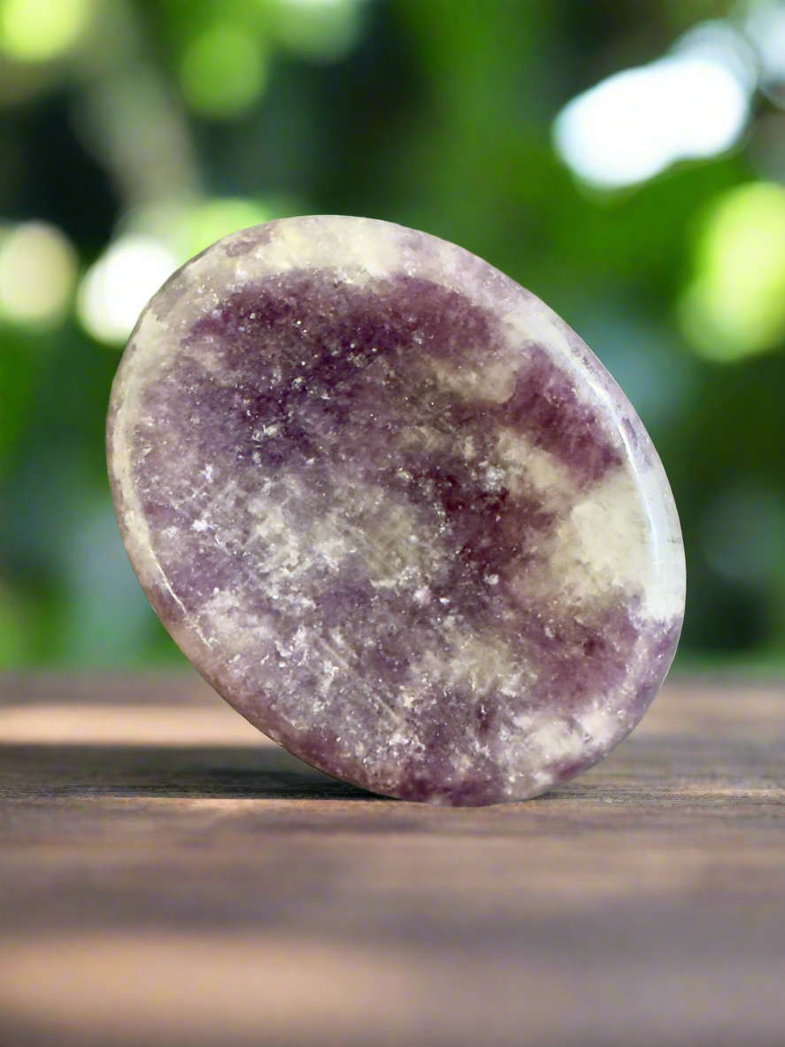 Oval, polished lepidolite stone on a wooden surface.
