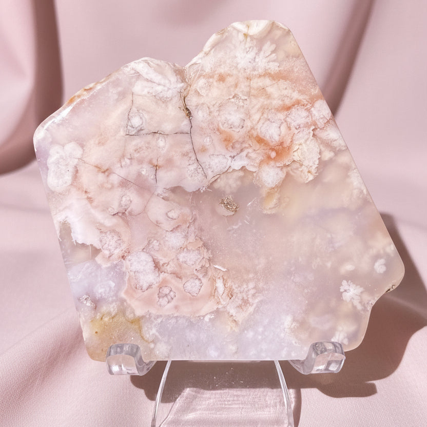 A pink and white flower agate crystal slab with  natural fissures, displayed on a clear acrylic stand  