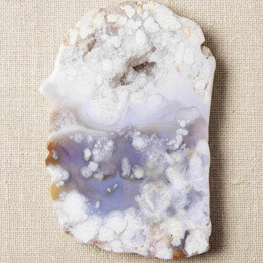 A raw flower agate geode slab with a white and lavender-purple banded pattern and crystalline formations