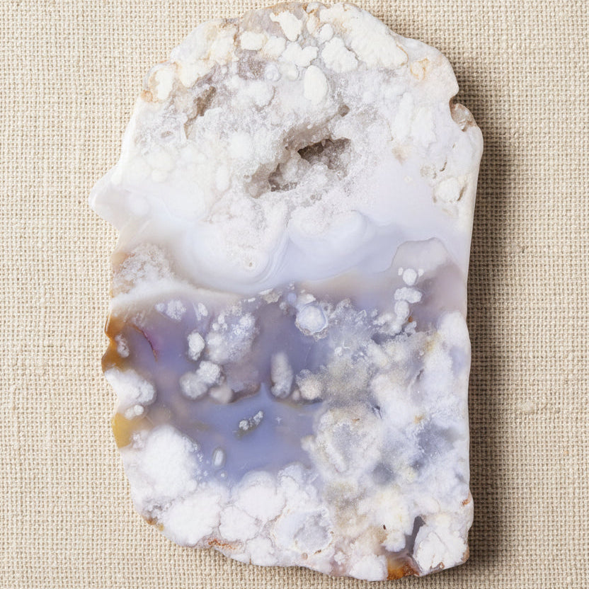 A raw flower agate geode slab with a white and lavender-purple banded pattern and crystalline formations
