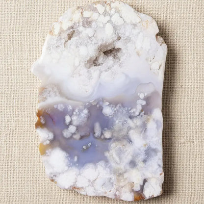 A raw flower agate geode slab with a white and lavender-purple banded pattern and crystalline formations