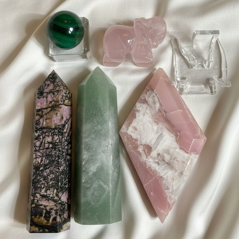 Close up of gemosophy compassion set, rhodonite tower, green aventurine tower, pink opal diamond shape, carved rose quartz elephant, malachite sphere with glass stand and acrylic stand 