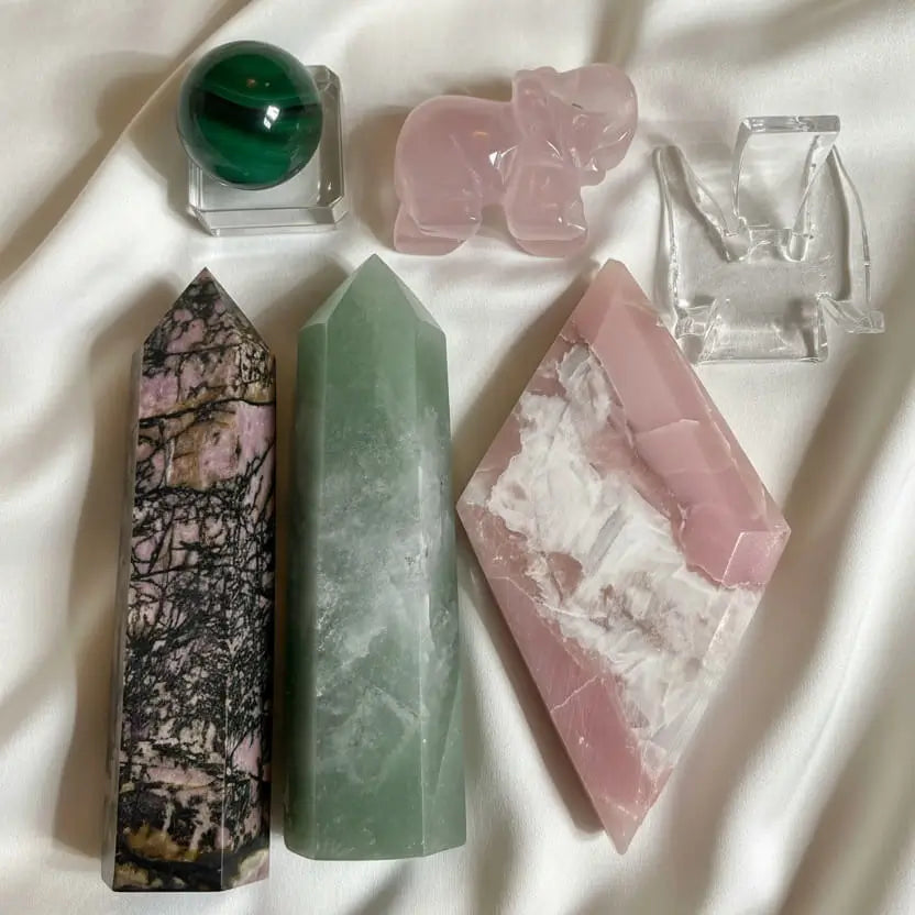 Close up of gemosophy compassion set, rhodonite tower, green aventurine tower, pink opal diamond shape, carved rose quartz elephant, malachite sphere with glass stand and acrylic stand 