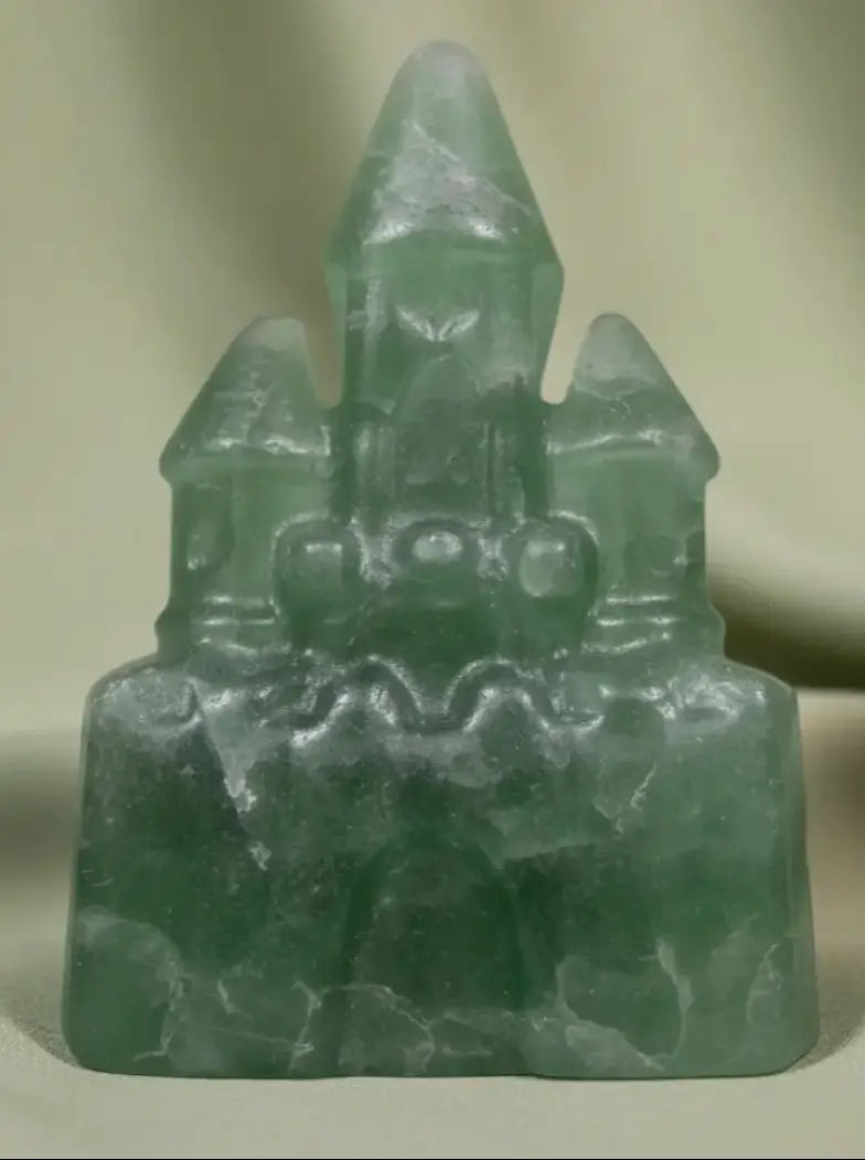 close up photo green carved fluorite castle light and dark greens three story castle, with a soft green background