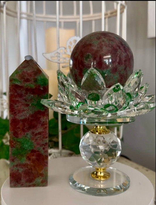 A crystal ball resting in a lotus flower shaped crystal holder, next to a crystal tower, on a white surface.