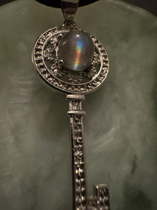 Silver key pendant with a round iridescent stone.
