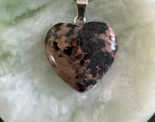 Heart-shaped pendant with a silver chain on a light green surface.