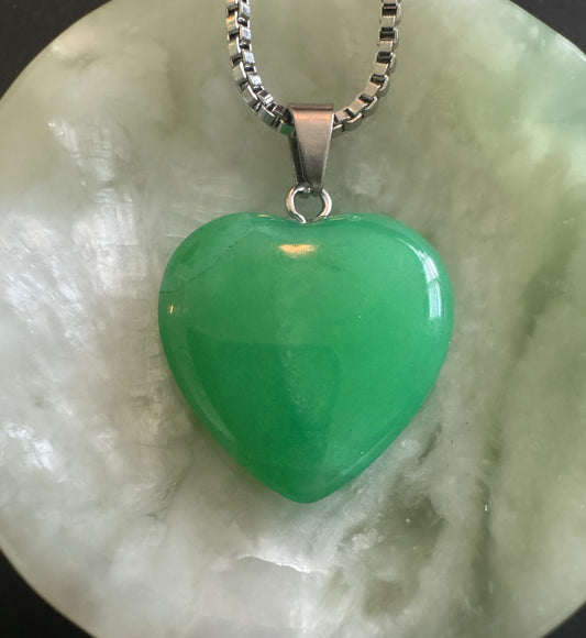Green heart-shaped necklace on jade background.
