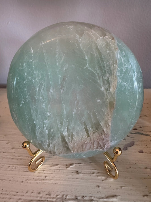 Round, green-toned, polished fluorite sphere on a gold metal spiral stand.
