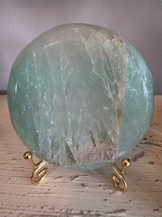 Round, green-toned, polished fluorite sphere on a gold metal spiral stand.
