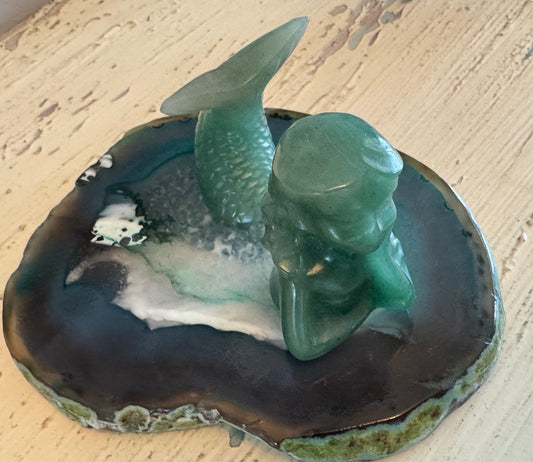 Two green gemstone mermaid figurines on a blue and white geode.