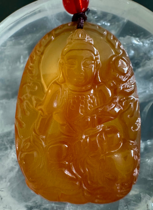 Yellow-orange jade pendant with carved seated figure.