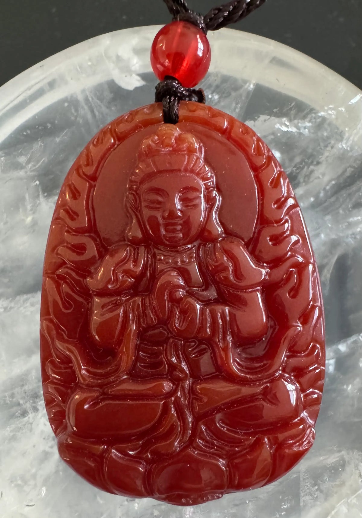 Red carved stone pendant with Buddha figure on black knotted cord with red bead.