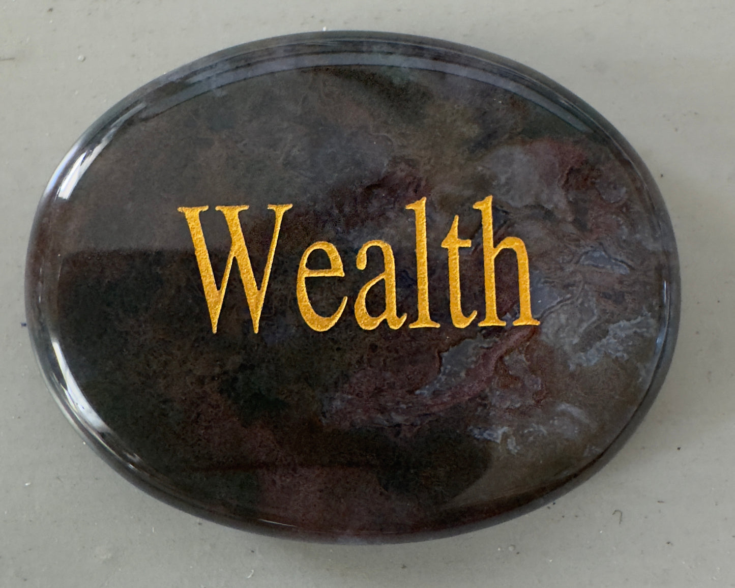 Oval, marble-like stone with gold "Wealth" lettering.