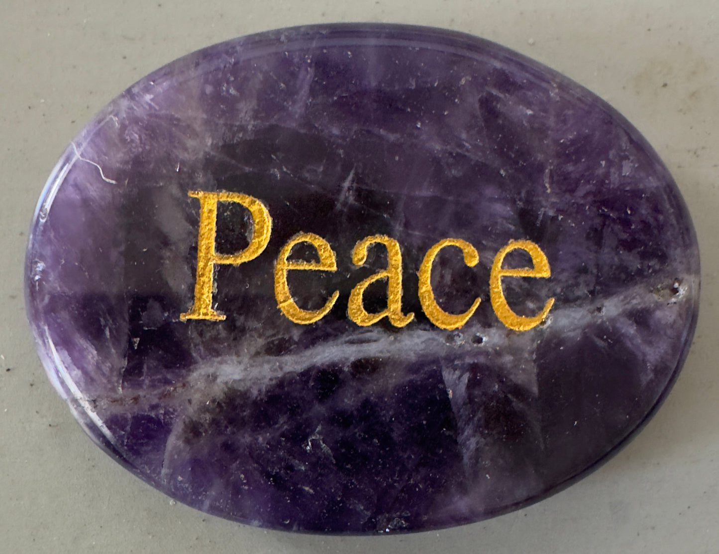 Oval, polished amethyst stone with the word "Peace" engraved in gold.