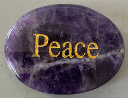 Oval, polished amethyst stone with the word "Peace" engraved in gold.