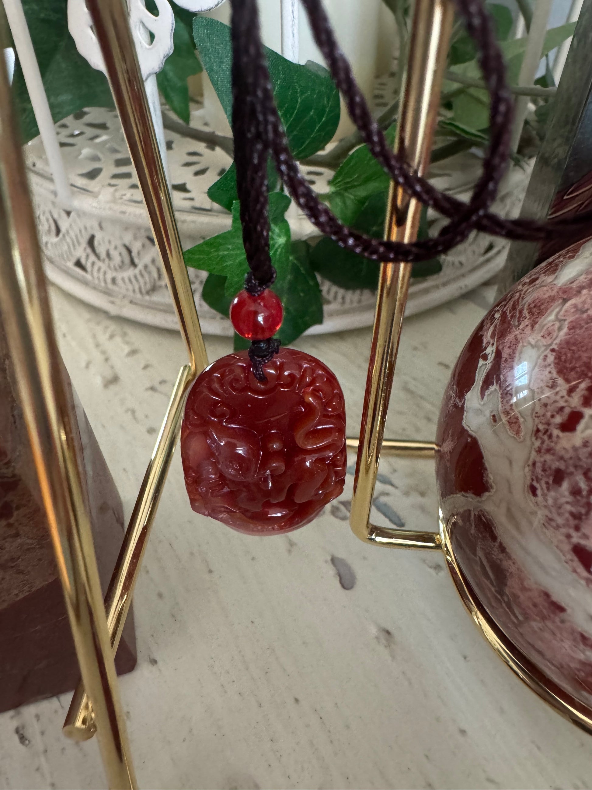 Red gemstone pendant with brown cord necklace.
