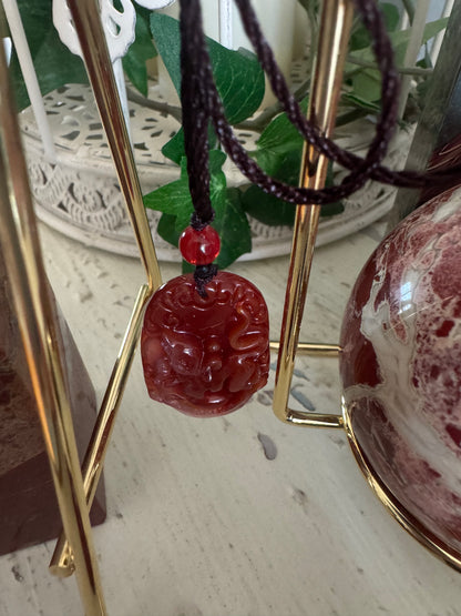 Red gemstone pendant with brown cord necklace.
