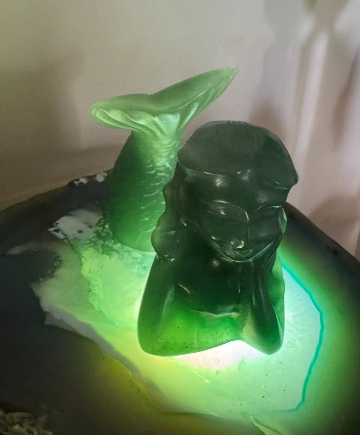 Green mermaid sculpture on illuminated agate.
