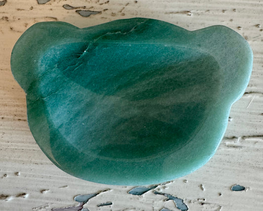Green bear-shaped gua sha tool on textured white surface.